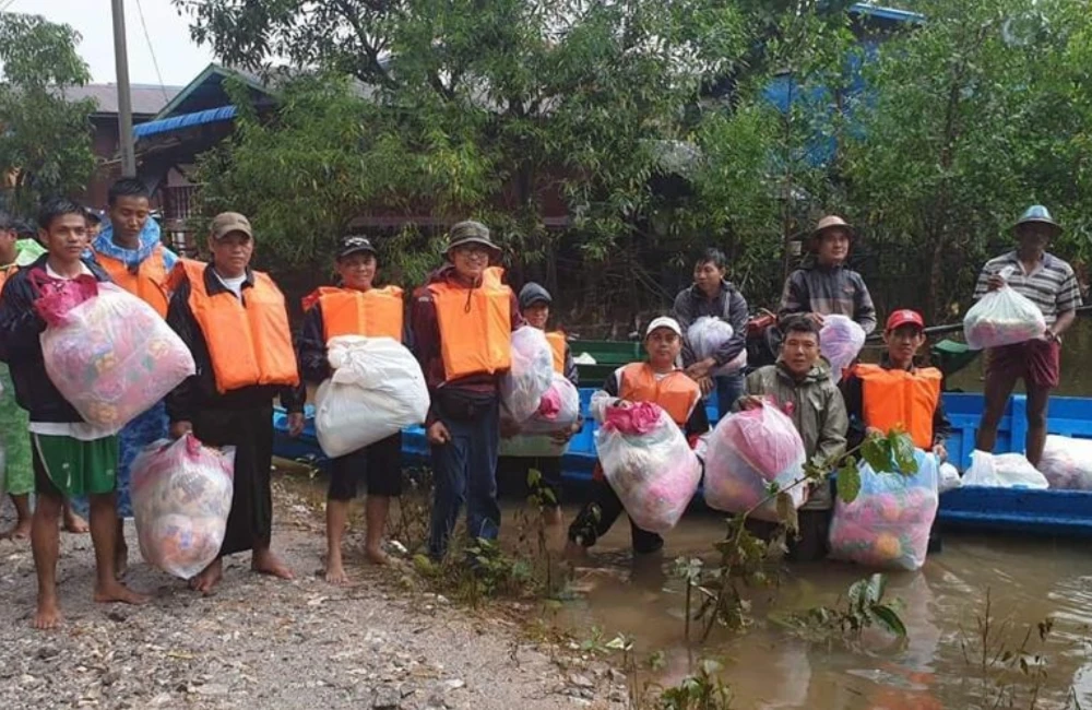 Relief workers standing in boat and water holding relief supplies